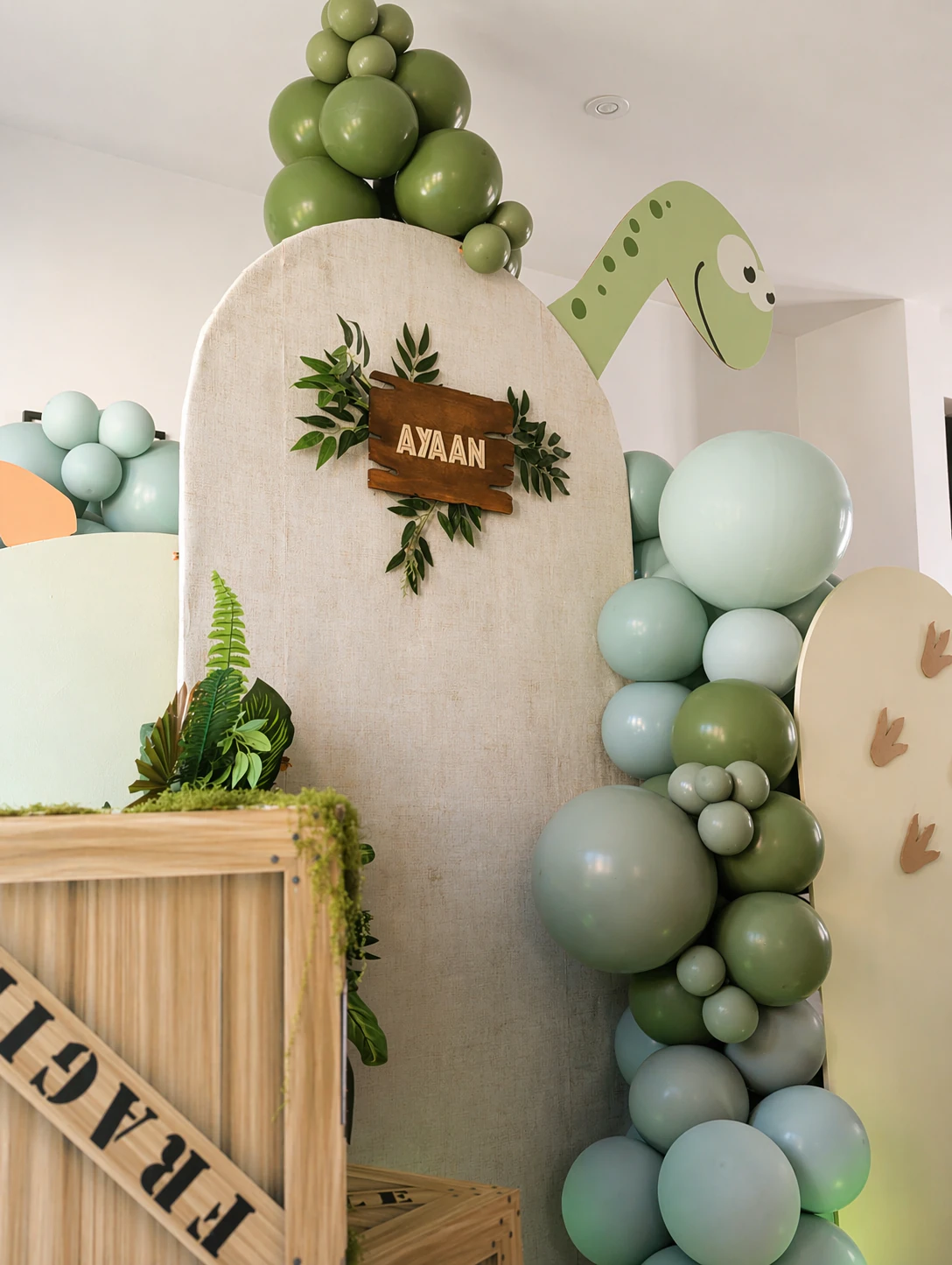 Close-up portrait of Ayaan's dinosaur arch - sage and cream balloons with tropical foliage and personalised signage by River Fox Events