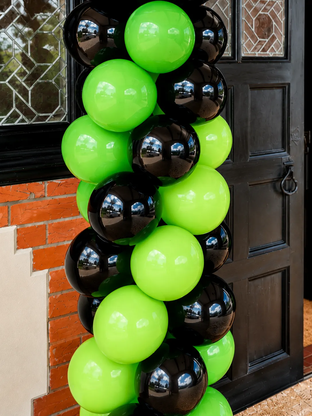 Close-up of stacked green and black balloons on the NXTGEN column against a black panelled door and brick wall