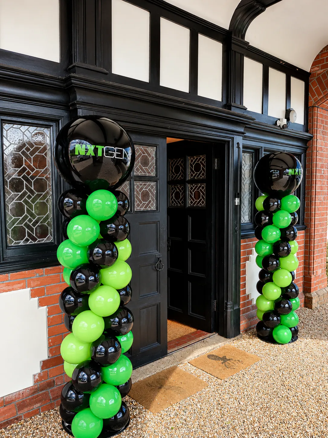 NXTGEN branded balloon columns in green and black flanking a black panelled doorway at a corporate entrance