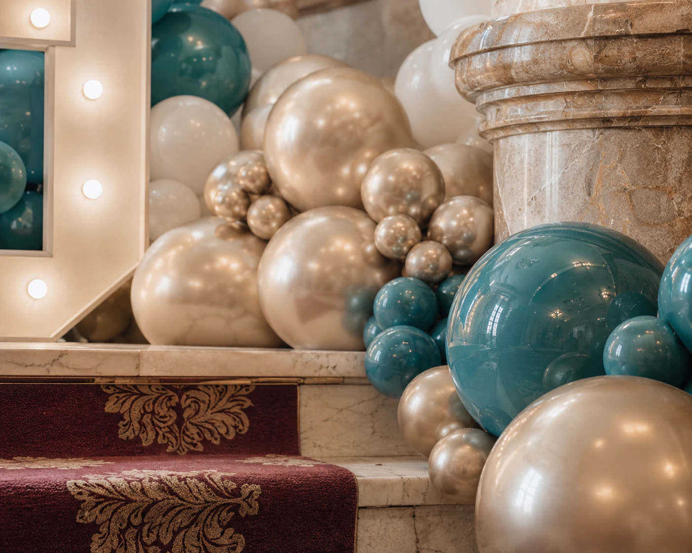 Close-up of cream, gold and pearl balloon detail beside the 125 anniversary marquee on a theatre staircase styled by River Fox Events