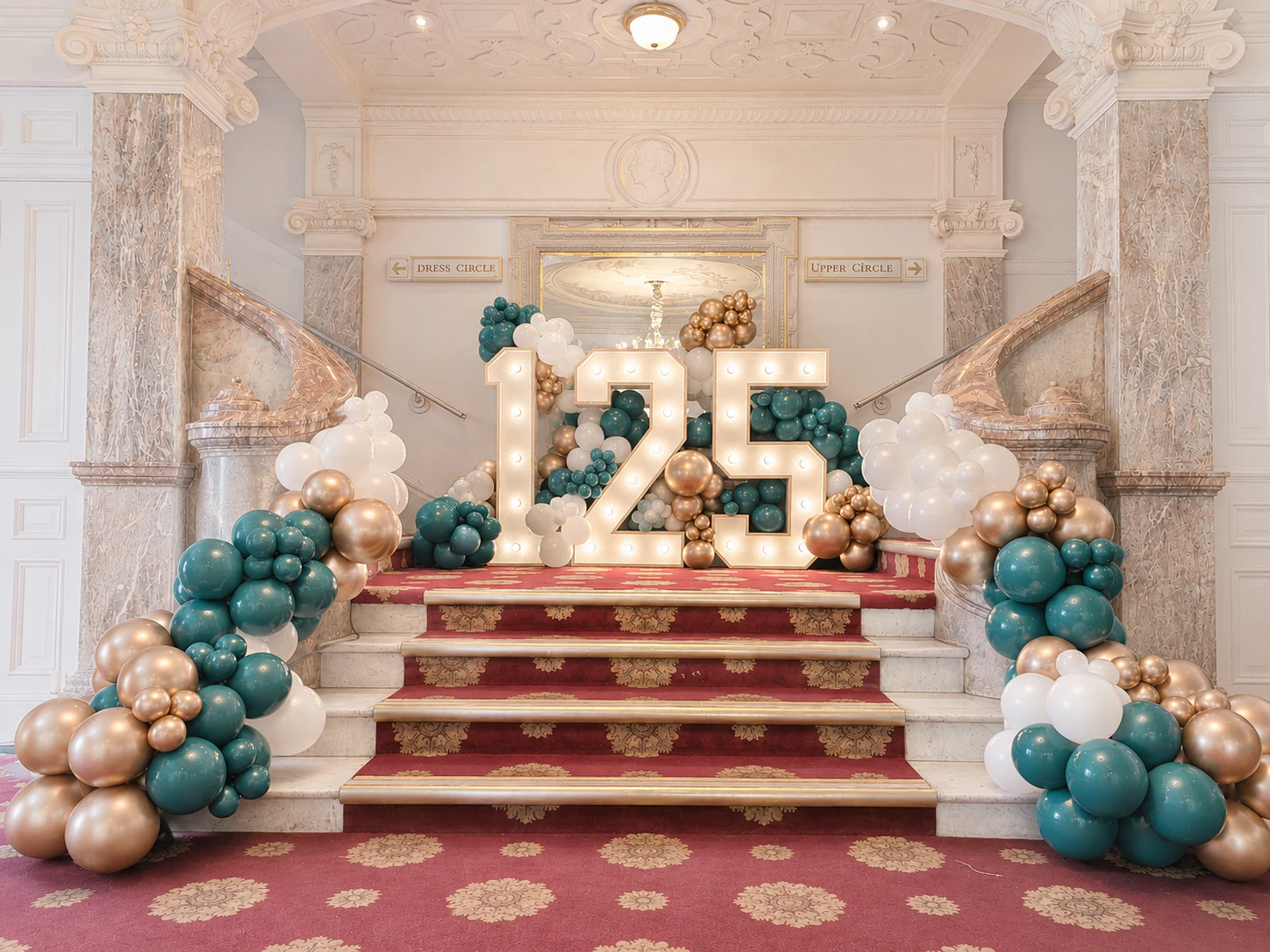 125th anniversary light-up marquee numbers on a theatre staircase with cream and gold balloons styled by River Fox Events for a Surrey corporate milestone