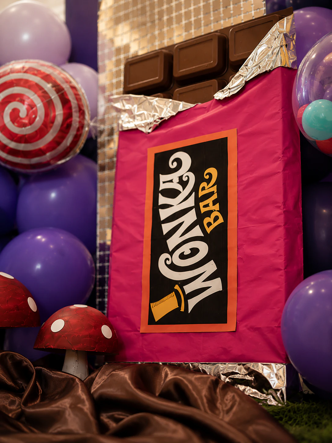 Close-up of the oversized chocolate-bar prop with lilac balloons, lollipop foil and mushroom props from Savanna's Willy Wonka fifth birthday styled in Surrey by River Fox Events